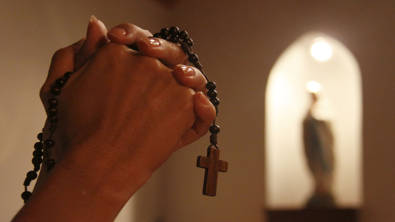 Praying hands holding the Rosary.